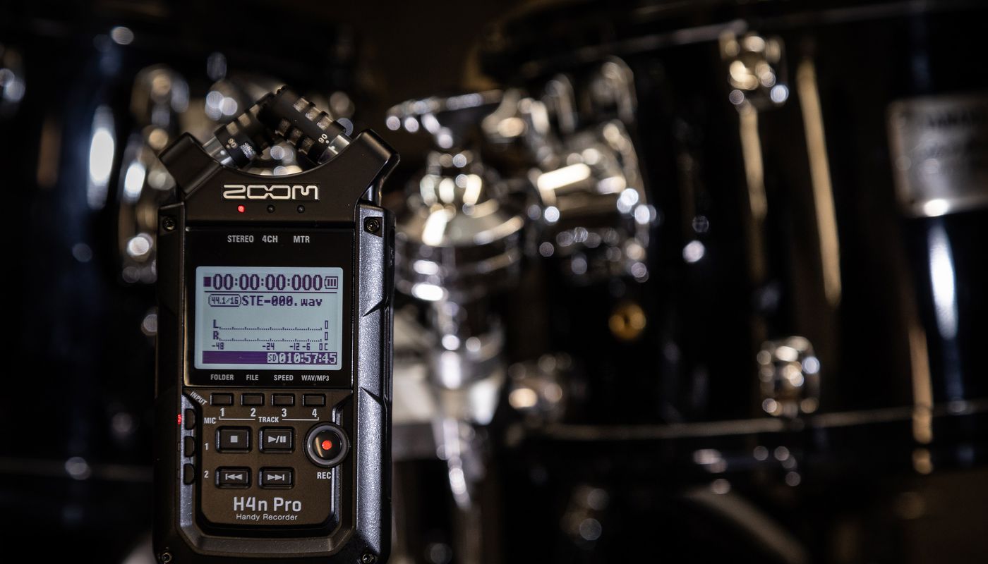 A guitarist and a bassist in a living room recording a song on the H4n Pro.