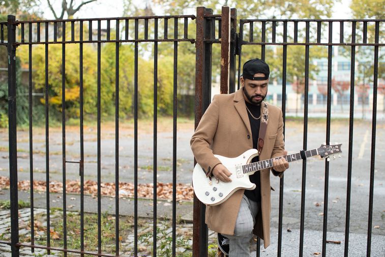 Ricardo Ramos playing guitar outside perched on a fence