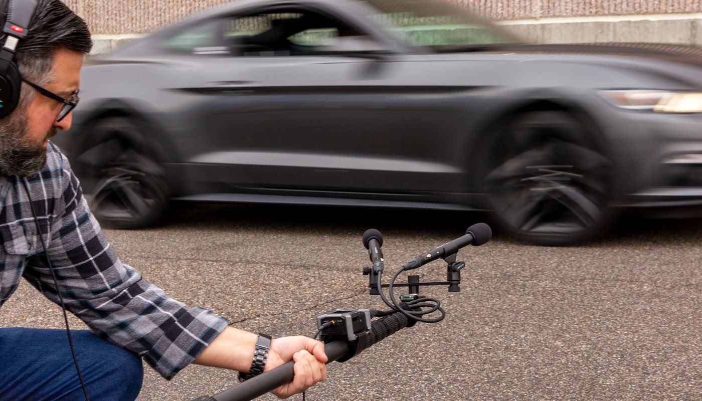 Sound man recording an automobile with boom pole and ZPC-1 mics on a stereo bar in the field